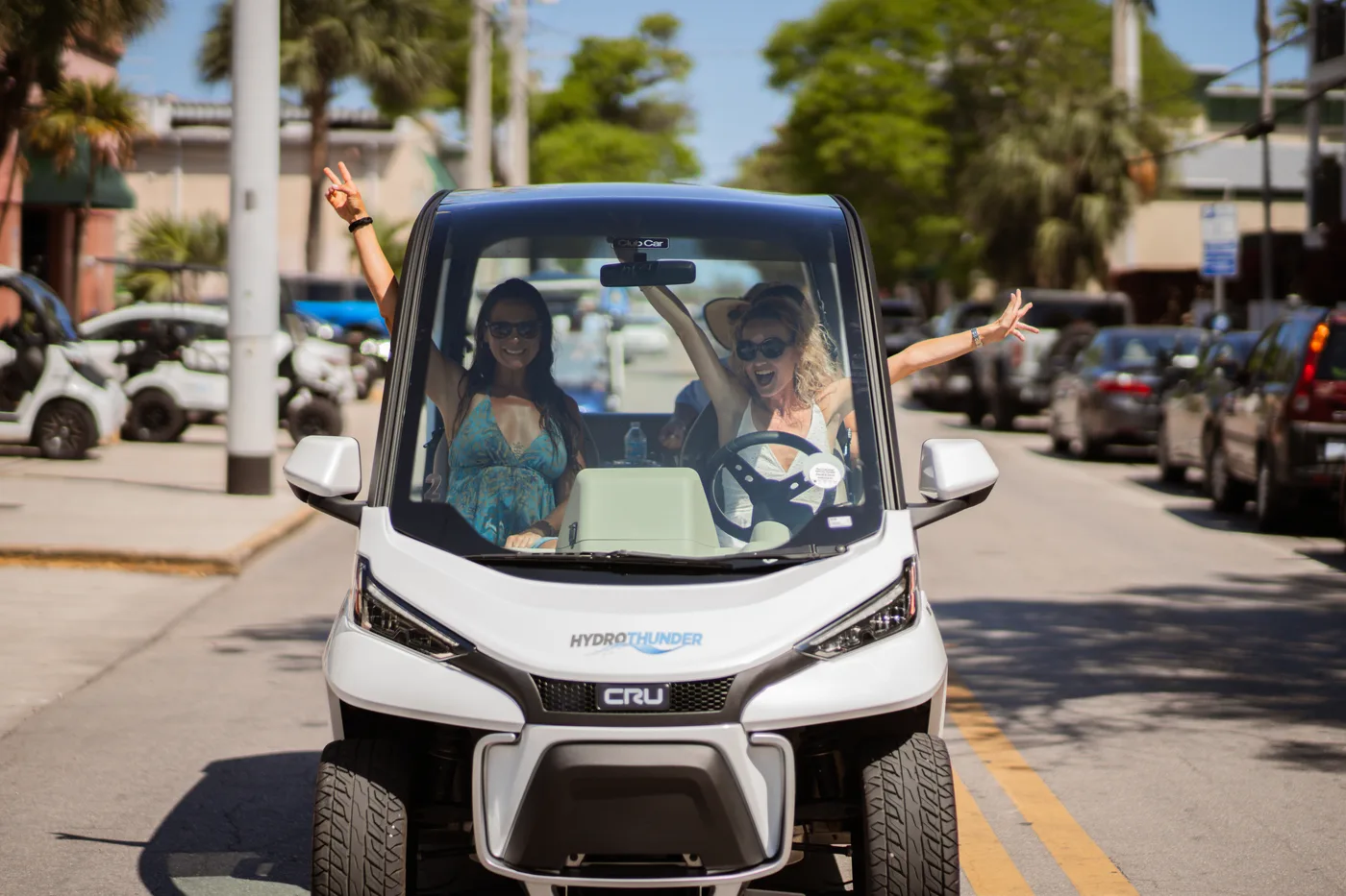Two women cheering in a CRU electric car on a Key West street
